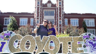 Student by Coyote move-in sign with parent