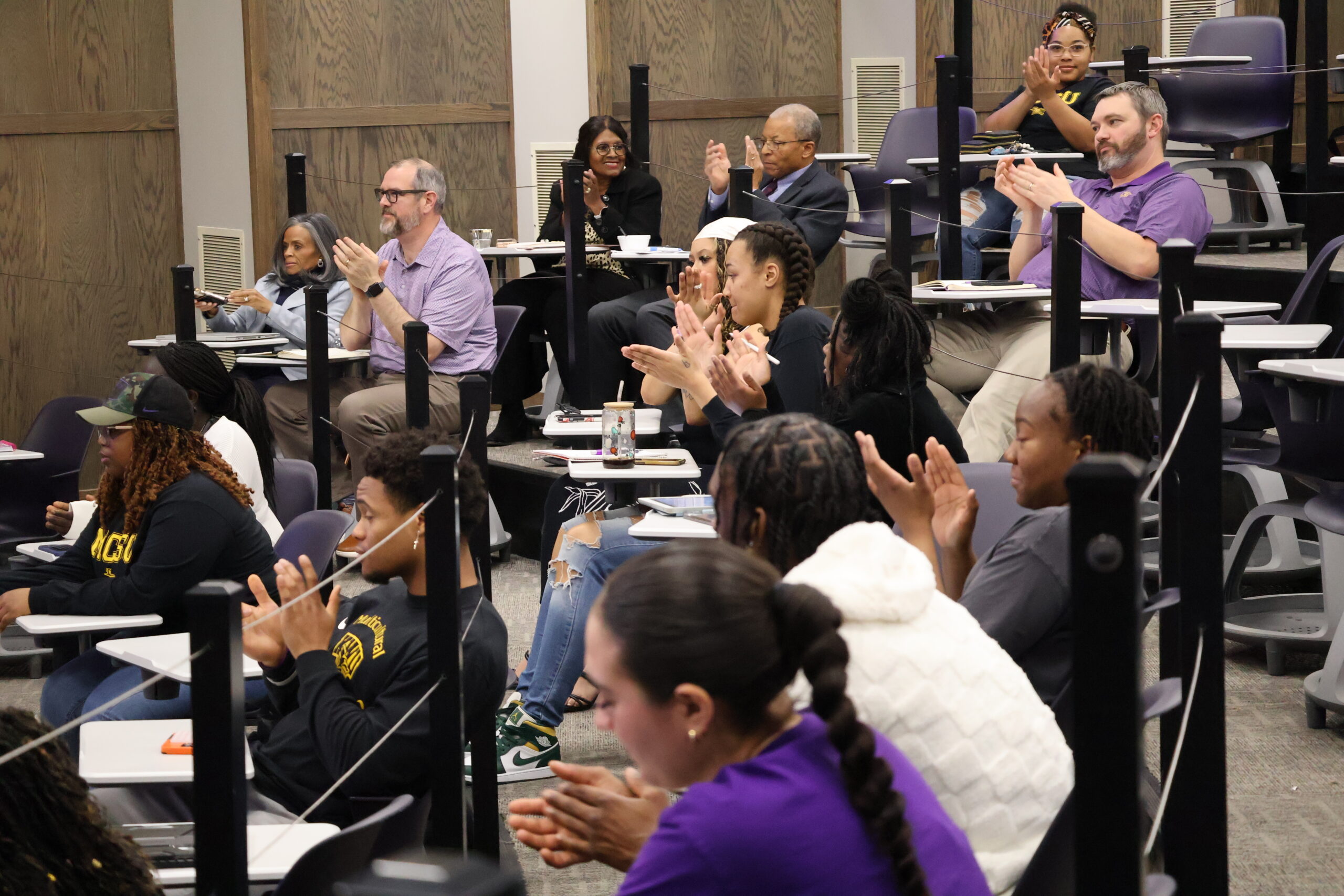 Group of people applauding while sitting in chairs in room