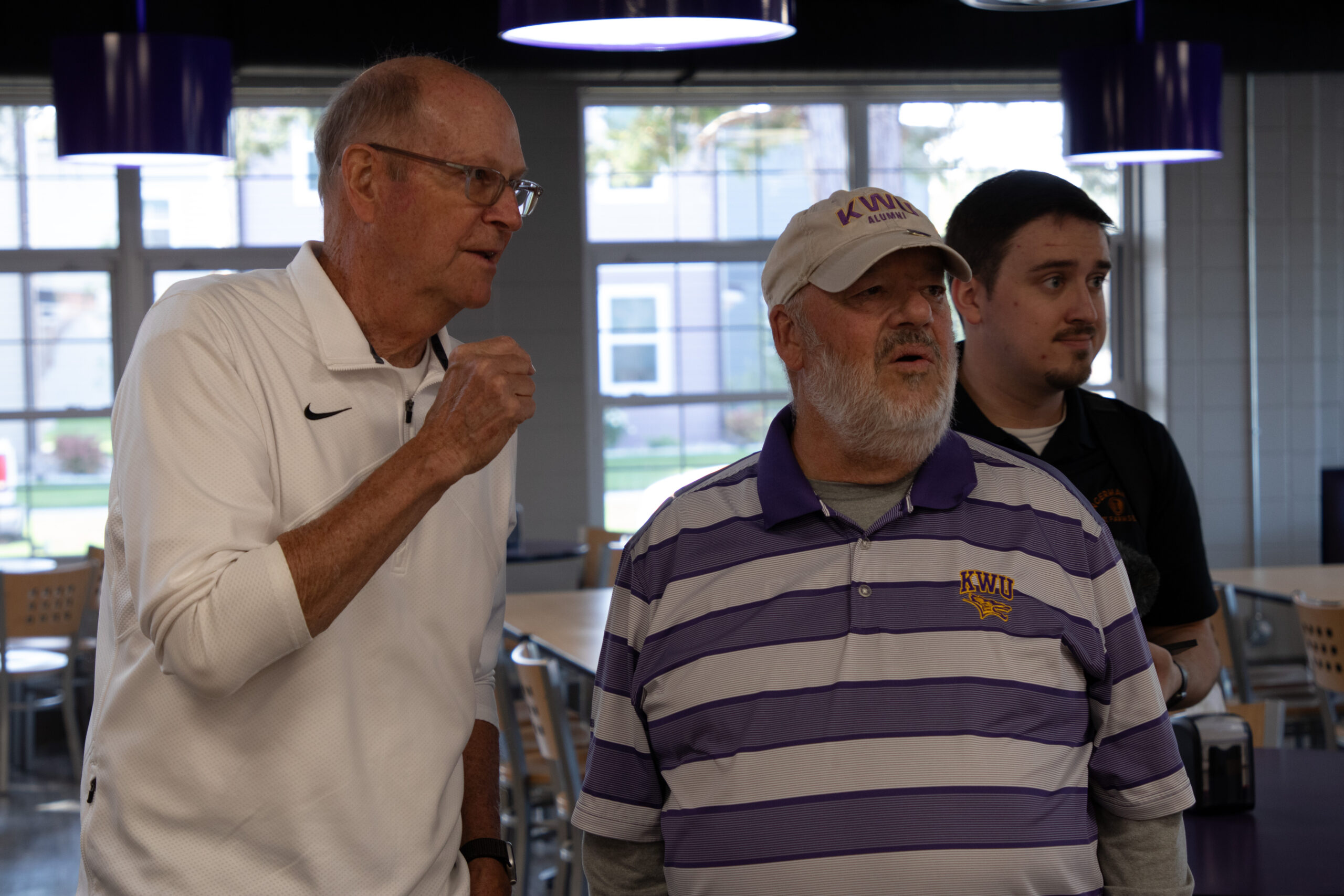 Two men speaking about something to side of photograph, third man surprised